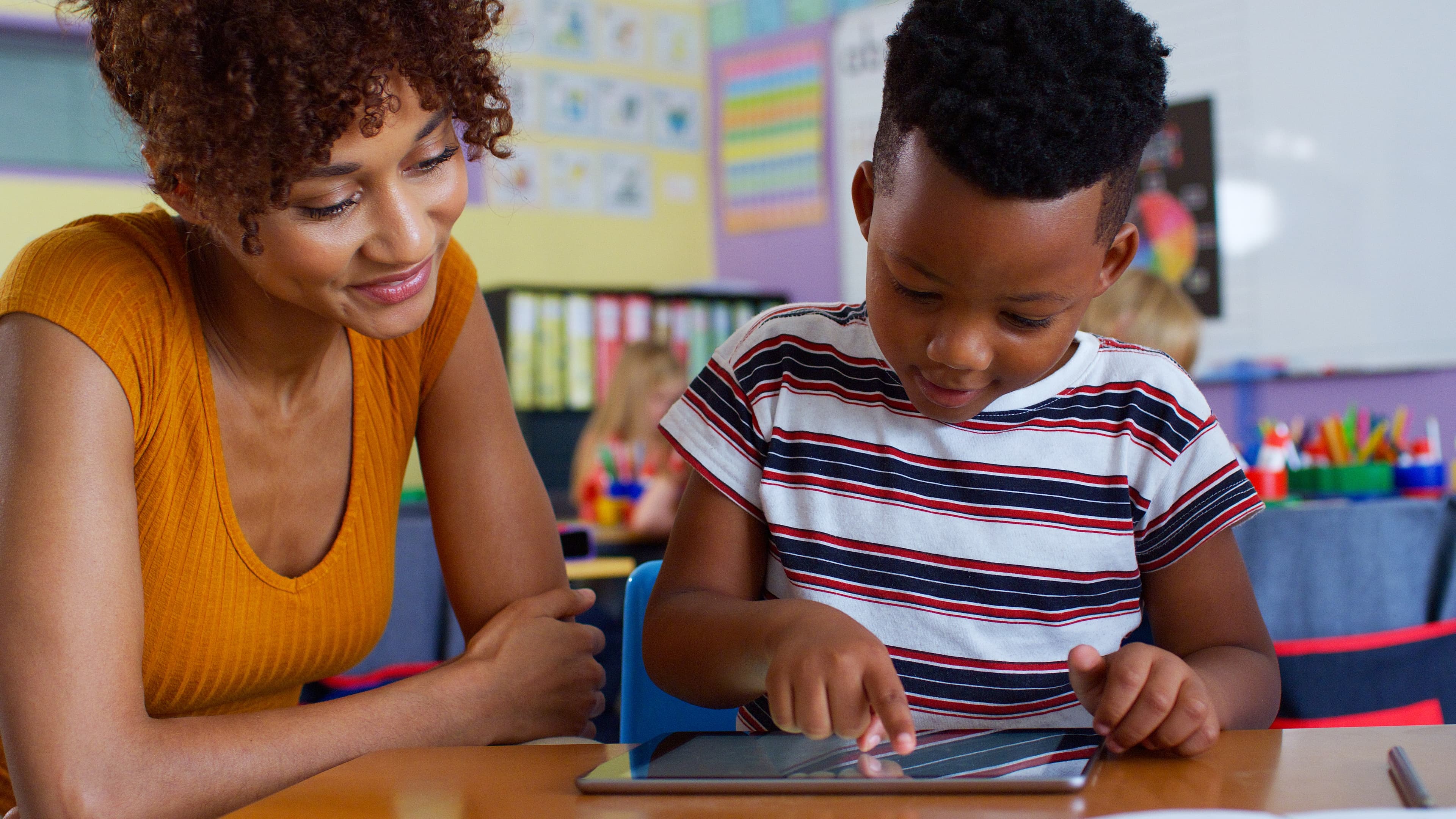 Teacher providing one-on-one tablet instruction to student in classroom