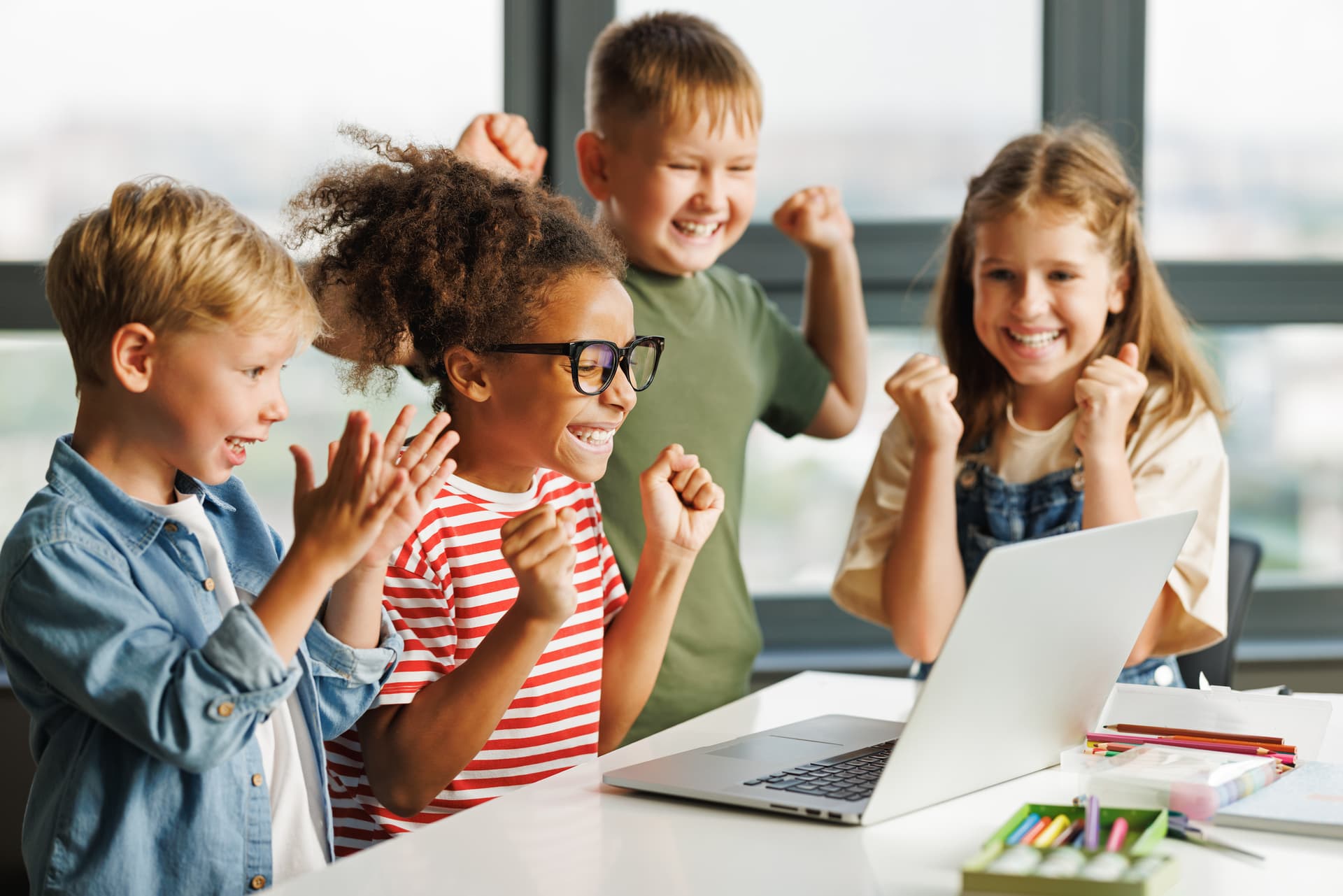 Primary school students celebrating success while learning on a laptop in the classroom